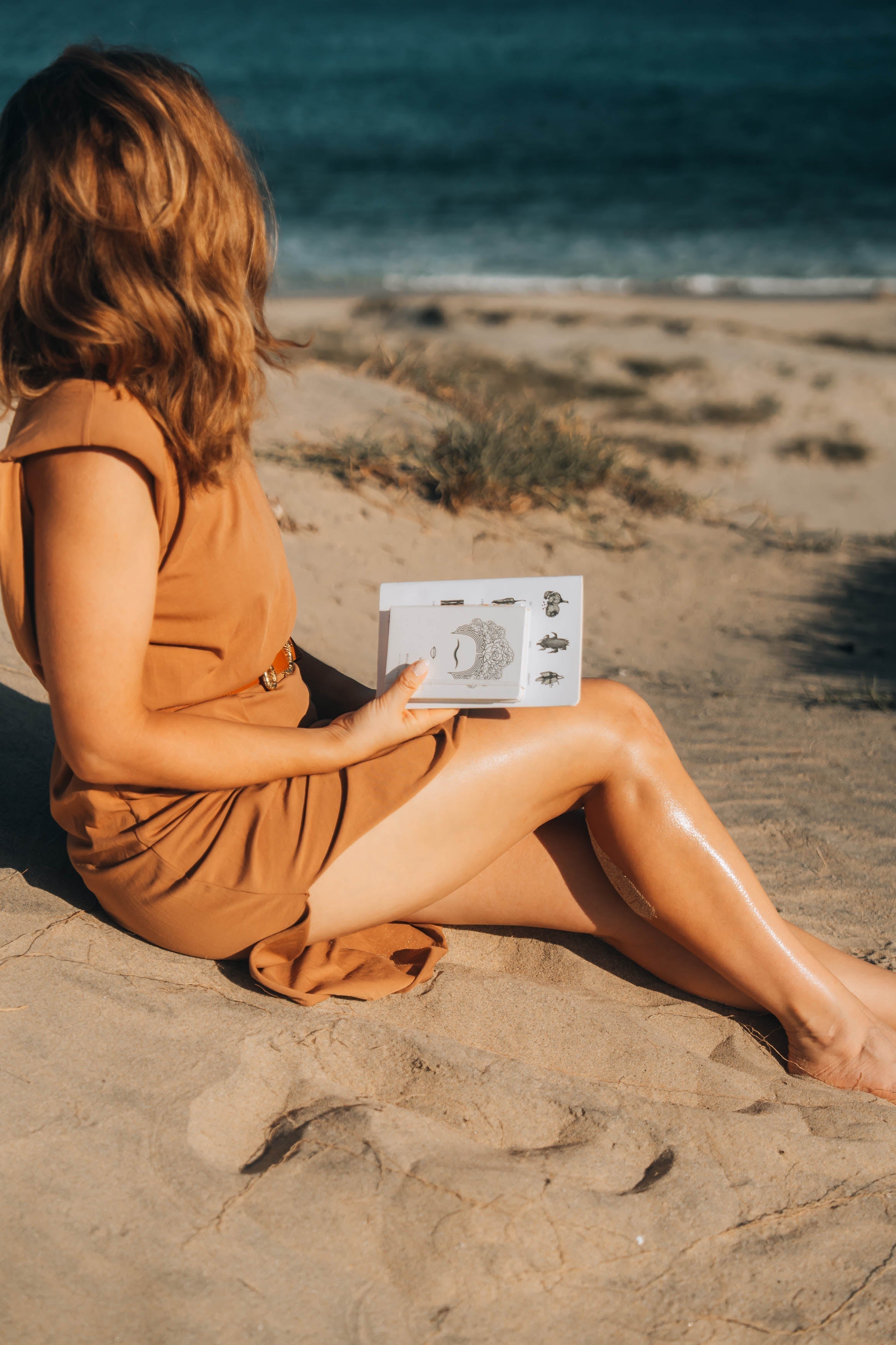 a woman writing on the beach and holding notebooks