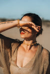 Woman in a golden knit top shading her eyes, wearing a gold beaded choker and bracelet from Waves of Light