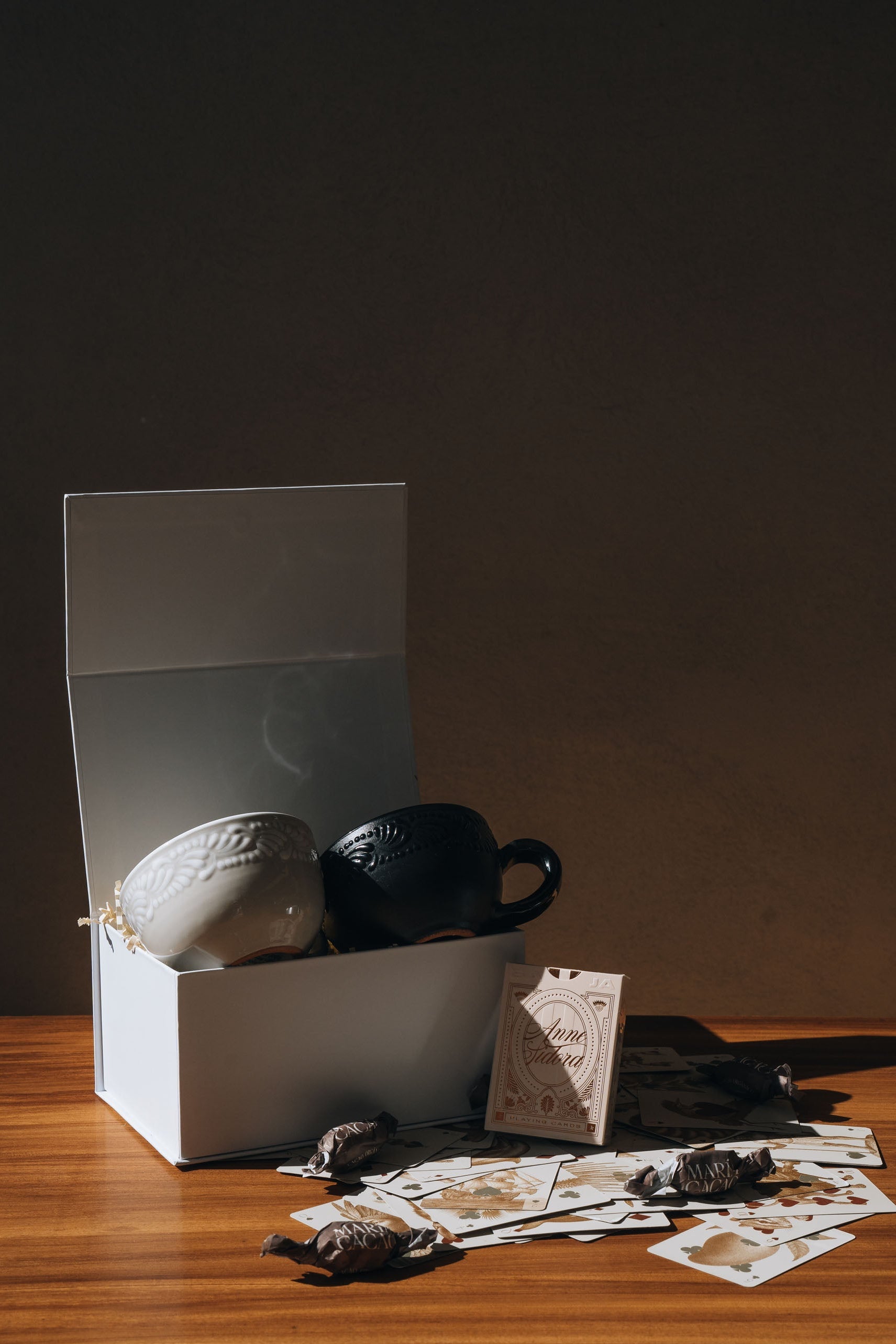 Tea or coffee set with a black cup, white cup, and a deck of cards on a wooden table.