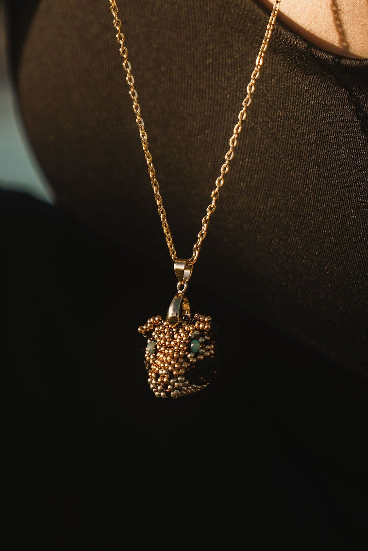 Close-up of a person wearing a gold jaguar necklace with a pendant, with a blurred background.