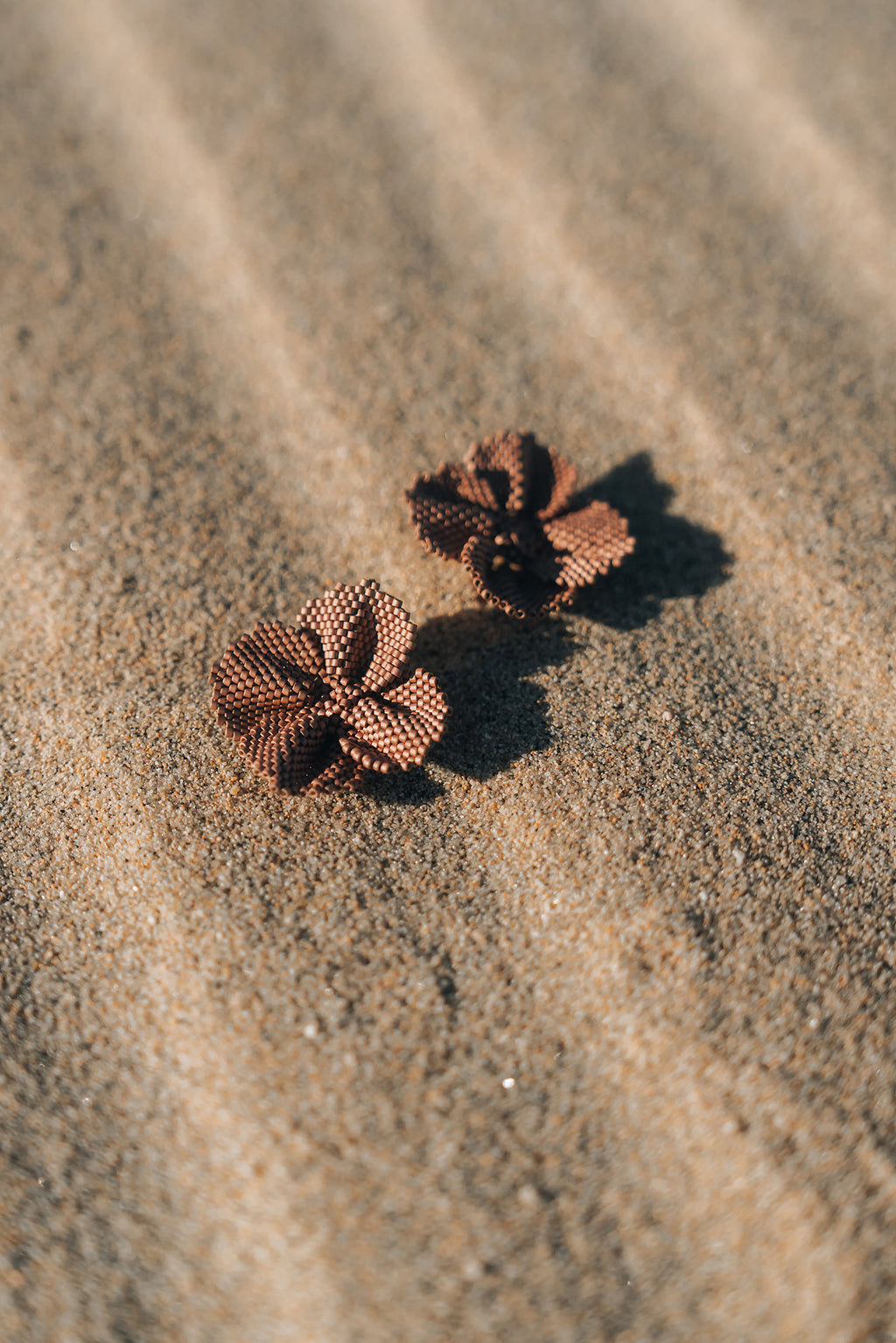 Two flower-shaped earrings on a sandy surface