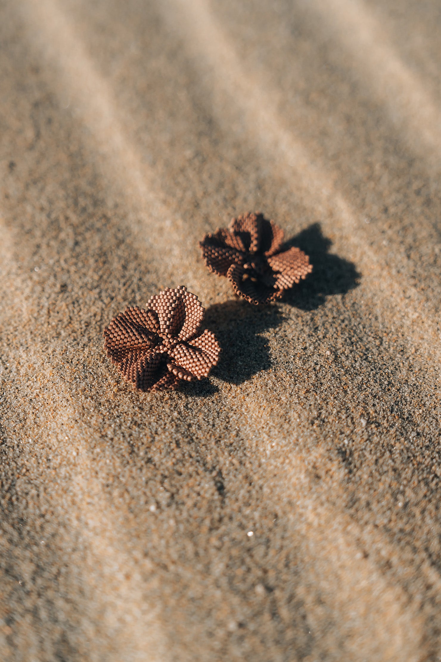 Two flower-shaped earrings on a sandy surface