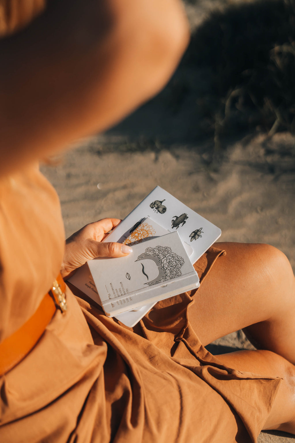 Person in a brown outfit holding notebooks on a beach