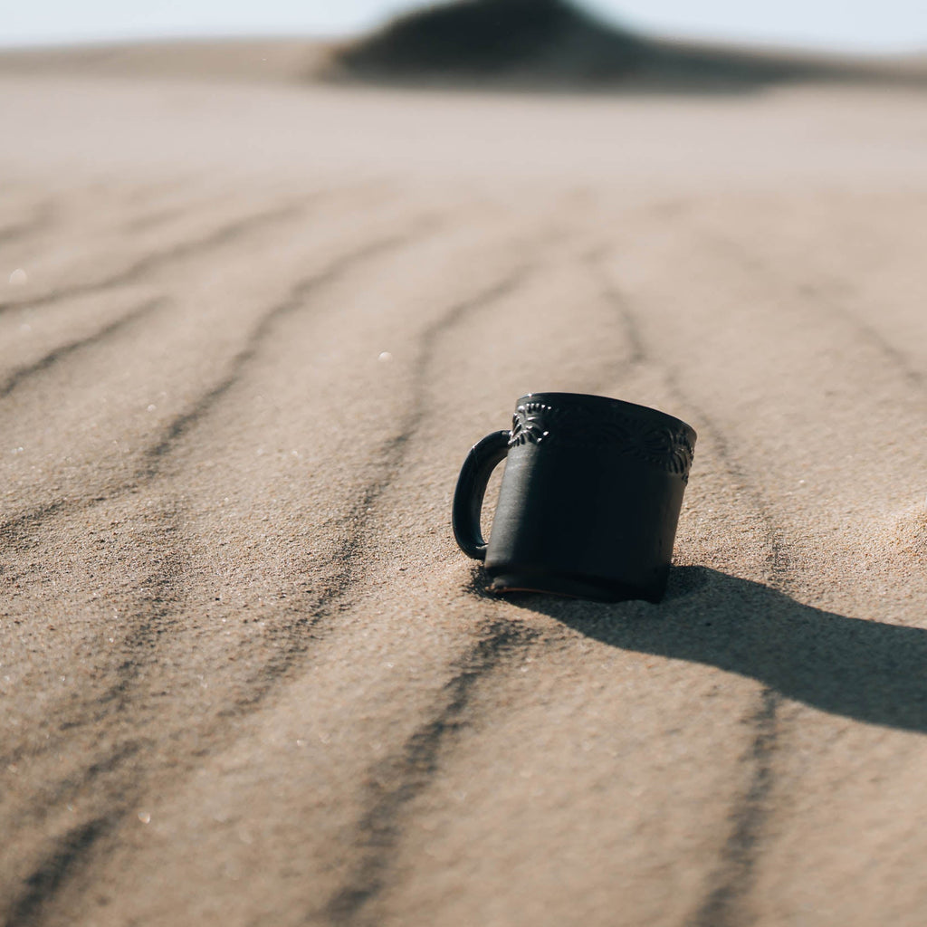 black mug in the sand
